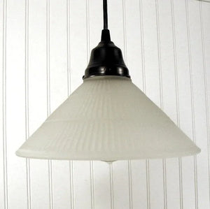 Frosted glass pendant light with ribbed texture, hanging against white paneled wall.
