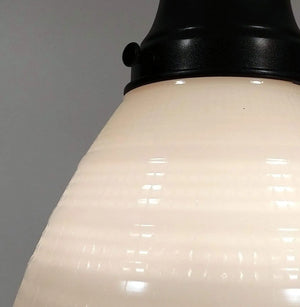 Close-up of a creamy off-white milk glass pendant light fixture with a waffle texture and black metal top.

