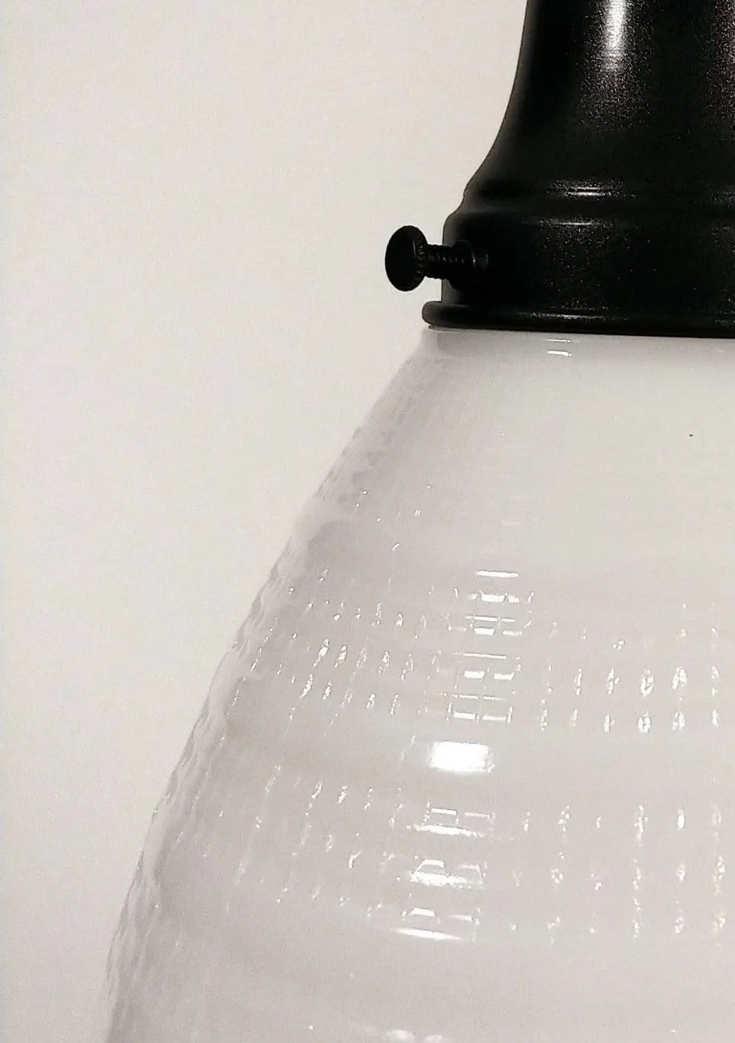 Close-up of a textured milk glass pendant light's white shade and black metal fitting.

