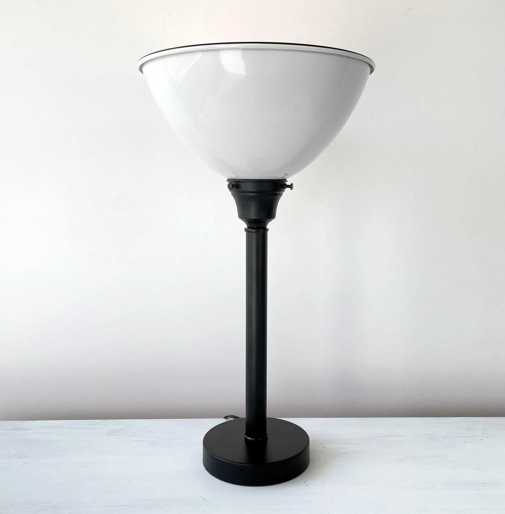 Black metal table lamp with a large, white, bowl-shaped shade; shown on a white surface.
