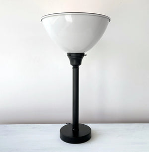 Black metal table lamp with a large, white, bowl-shaped shade; shown on a white surface.
