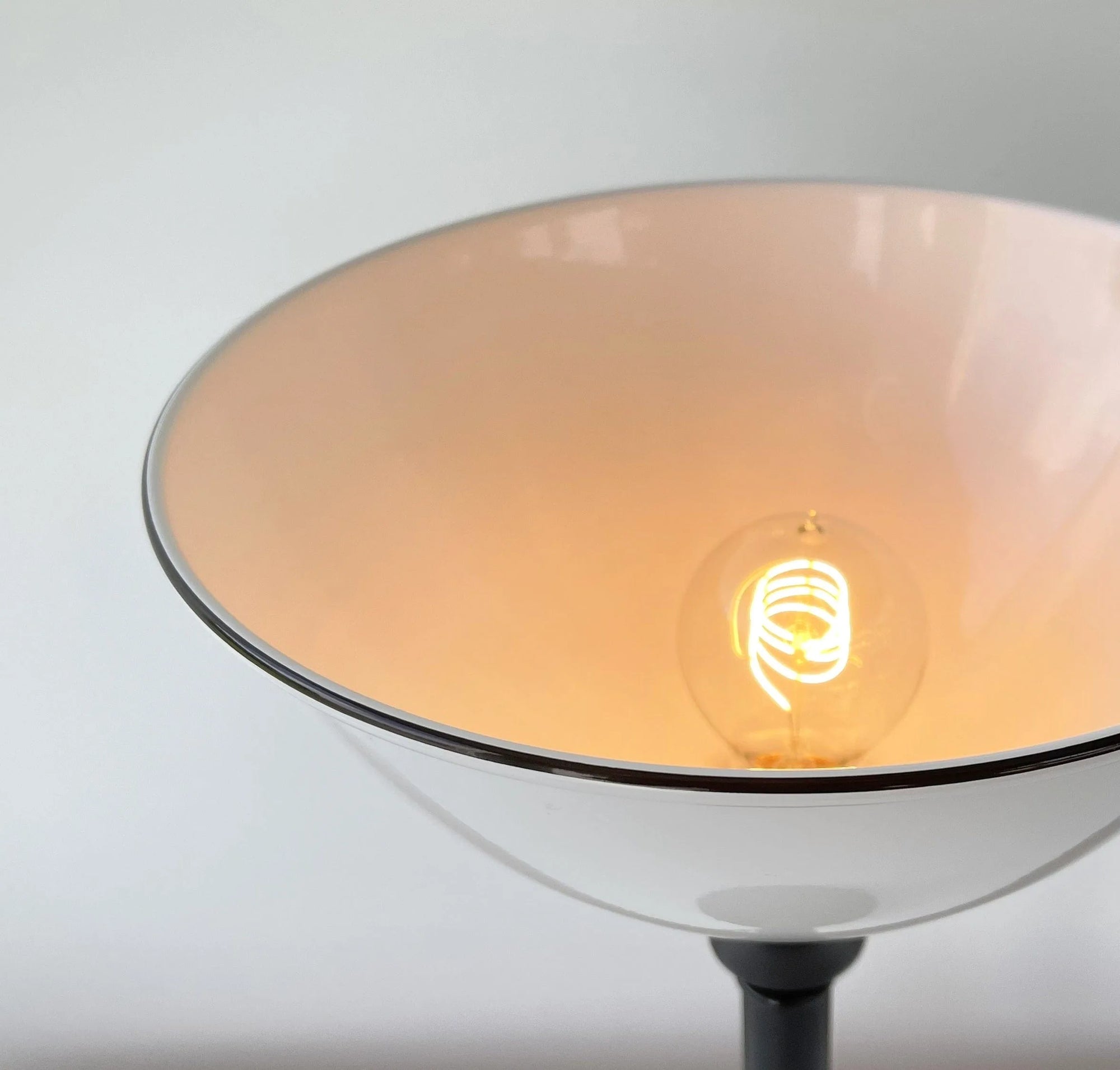 Illuminated white table lampshade with a dark base, showcasing an Edison bulb.
